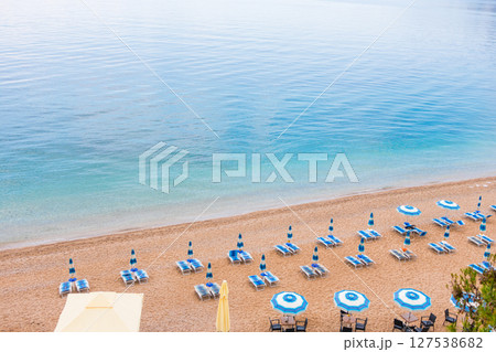 Tranquil morning at a beach with blue umbrellas and loungers. Coastal vacation, summer relaxation and peaceful seaside tourism. Tranquil morning at a beach with blue umbrellas and loungers. Coastal vacation, summer relaxation and peaceful seaside tourism. 127538682