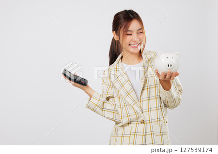 Holding both calculator and piggybank, the woman cross-verifies her tax and money goals using another calculator for finance and banking accuracy. isolated studio white background Holding both calculator and piggybank, the woman cross-verifies her tax and money goals using another calculator for finance and banking accuracy. isolated studio white background 127539174