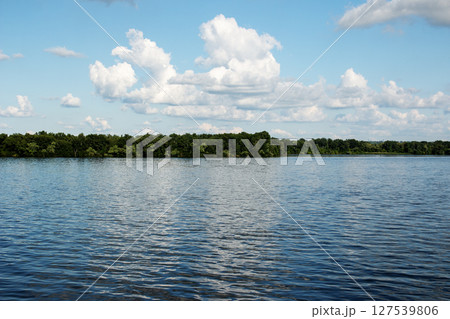 Panoramic view of the Dnieper river bank from the embankment of the city of Dnieper. Reflection of sky with clouds on the surface of the water. Panoramic view of the Dnieper river bank from the embankment of the city of Dnieper. Reflection of sky with clouds on the surface of the water. 127539806