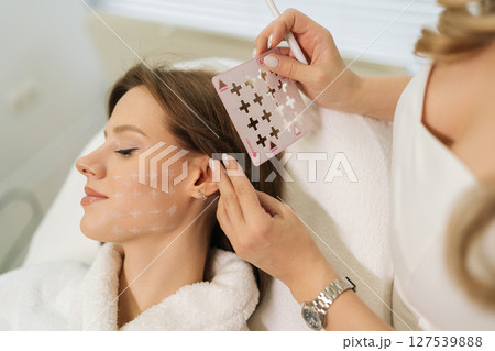 Close-up of beautician preparing patient facial skin for treatment marking grid with white pencil in modern beauty clinic. Concept of non-surgery cosmetology, professional skincare, beauty treatment. 127539888