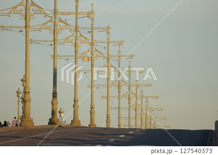 rows of lampposts and poles with electric grids for a tram on an Troitskiy Bridge at sunset rows of lampposts and poles with electric grids for a tram on an Troitskiy Bridge at sunset 127540373