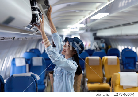 female passenger keep bag in the compartment above the seat in the plane. travel concept 127540674