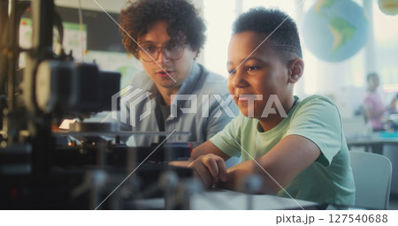Talented Boy Sitting at the Table with Teacher, Studying Printing on Advanced 3D Printer 127540688