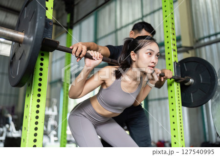 Partner Workout. Woman squatting with support from trainer in gym. 127540995