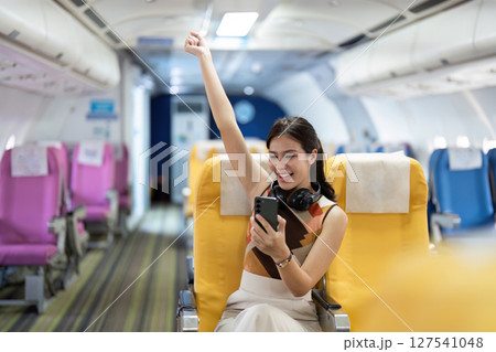 Joyful Traveler Using Smartphone on Airplane. Excited woman enjoying travel experience with headphones. 127541048