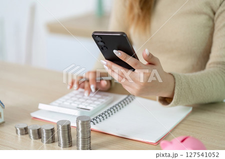 Digital Finance Management. Woman using smartphone while budgeting with coins. Digital Finance Management. Woman using smartphone while budgeting with coins. 127541052