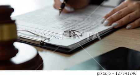 Divorce Agreement Signing. A lawyer completing a divorce contract with wedding rings in focus. Divorce Agreement Signing. A lawyer completing a divorce contract with wedding rings in focus. 127541246