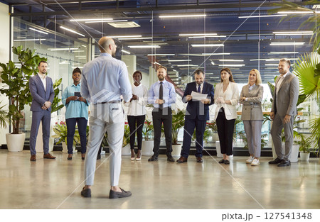 Diverse team of company employees standing in row, listening to business leader or coach on meeting. 127541348