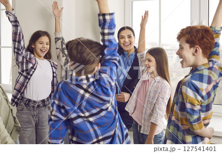 Group of happy junior school students raising hands together while standing in classroom 127541401