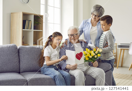 Happy grandfather receives a greeting card and a bouquet of flowers from his family Happy grandfather receives a greeting card and a bouquet of flowers from his family 127541441
