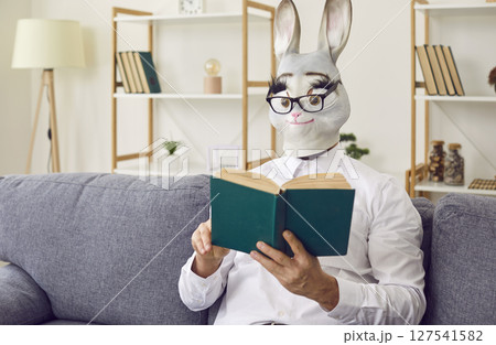 Strange man wearing a funny rabbit mask is sitting on the couch and reading a book 127541582
