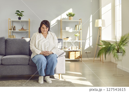 Depressed overweight woman sitting on sofa at home Depressed overweight woman sitting on sofa at home 127541615