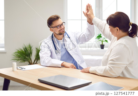 Young happy male doctor giving high five to a fat patient reaching great results in treatment. Young happy male doctor giving high five to a fat patient reaching great results in treatment. 127541777