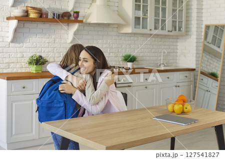 Loving mother giving hug to small pupil child, warm embrace before school day in modern kitchen Loving mother giving hug to small pupil child, warm embrace before school day in modern kitchen 127541827