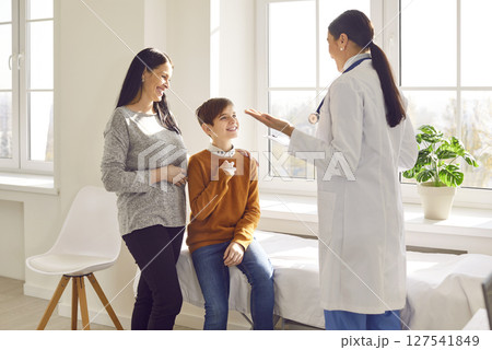 Woman pediatrician examining preteen boy patient who came with his mother 127541849