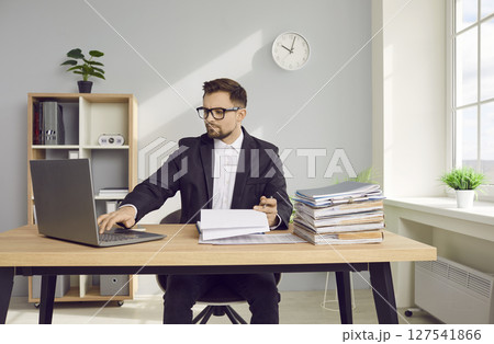 Young business man working at the desk with a pile of documents on his workplace at office. Young business man working at the desk with a pile of documents on his workplace at office. 127541866