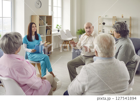 Group of senior men and women sitting in a circle in nursing home with a young nurse. Group of senior men and women sitting in a circle in nursing home with a young nurse. 127541894