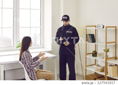 Police officer taking notes on clipboard while interviewing victim of house burglary 127541917