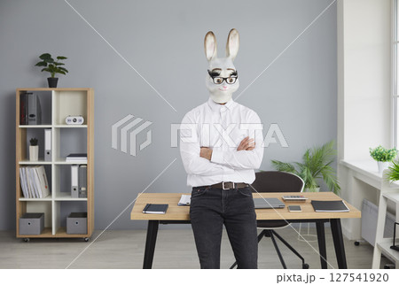 Businessman in rabbit head mask standing with folded hands in office Businessman in rabbit head mask standing with folded hands in office 127541920