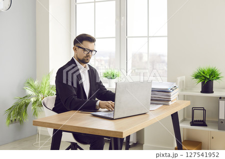 Focused confident businessman working with laptop in office 127541952
