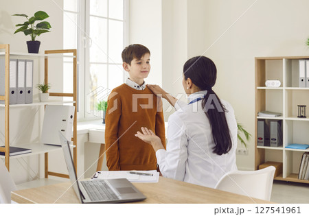 Smiling woman pediatrician examining preteen boy patient in medical office 127541961