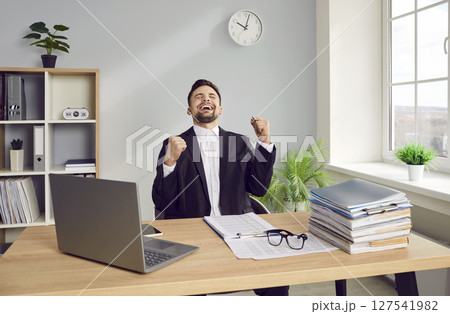 Business man sitting in the office making yes gesture with hands in fists like a winner. 127541982