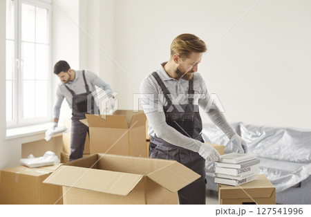 Movers male team packing, choosing cardboard box, arranging items carefully inside, preparing Movers male team packing, choosing cardboard box, arranging items carefully inside, preparing 127541996