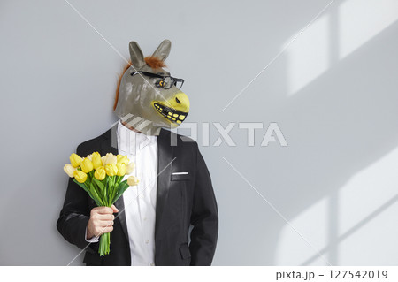 Unidentifiable man in rubber donkey head mask holding bouquet of flowers Unidentifiable man in rubber donkey head mask holding bouquet of flowers 127542019