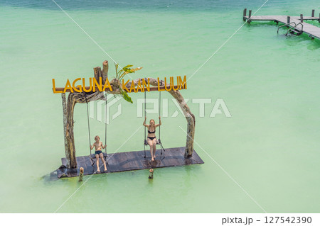 Mother and son swinging over the turquoise waters of Kaan Luum Lagoon, Quintana Roo, Mexico. Family bonding and tropical adventure concept 127542390