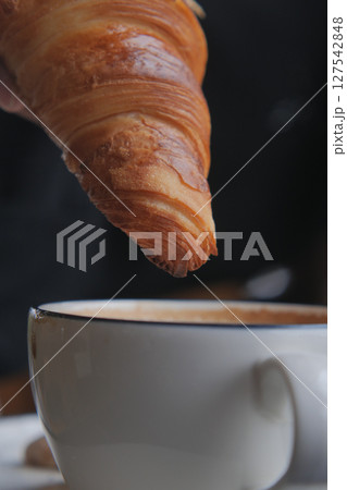 Croissant nearing cup of coffee in cozy cafe setting 127542848