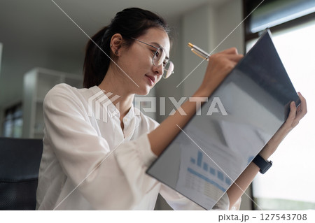 Portrait of an Asian woman working on folder in a modern office. Make an account analysis report Portrait of an Asian woman working on folder in a modern office. Make an account analysis report 127543708
