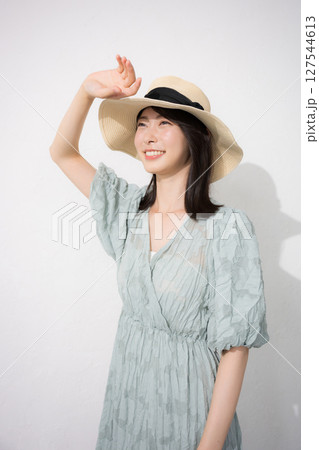 麦わら帽子を被って眩しい日焼けを気にする夏服の女性　白背景 127544613