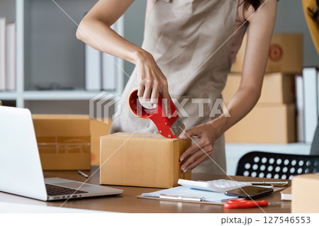 Young business entrepreneur sealing a box with tape. Preparing for shipping, Packing, online selling, e-commerce concept 127546553