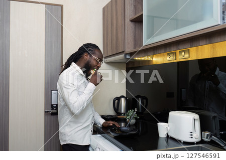 African businessman eat sandwich in the morning and use a tablet to work on company documents. While working online from home 127546591