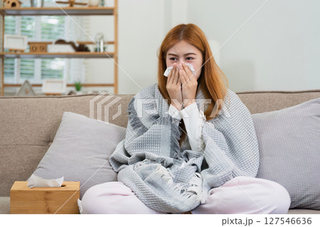 young woman sitting on sofa covered with blanket freezing blowing running nose got fever caught cold sneezing in tissue young woman sitting on sofa covered with blanket freezing blowing running nose got fever caught cold sneezing in tissue 127546636
