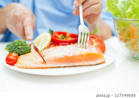 Asian elderly woman patient eating salmon stake and vegetable salad for healthy food in hospital. Asian elderly woman patient eating salmon stake and vegetable salad for healthy food in hospital. 127549089