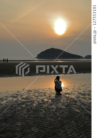 夕日が映る三豊父母ヶ浜の潮だまりを眺める女性 127553191