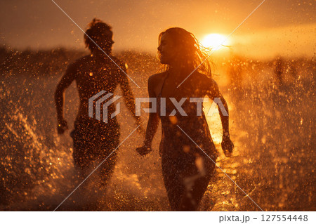 夕日の海で水遊びを楽しむカップルのシルエットと輝く水しぶき 127554448