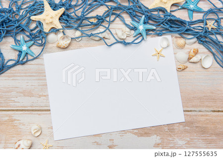 Fishing net, seashells and starfishes framing blank paper on wooden background 127555635