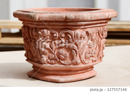Terracotta plant pot with floral carvings. Ornate garden container features elegant patterns, perfect for home or patio decor. Ideal for rustic or nature visuals. 127557148
