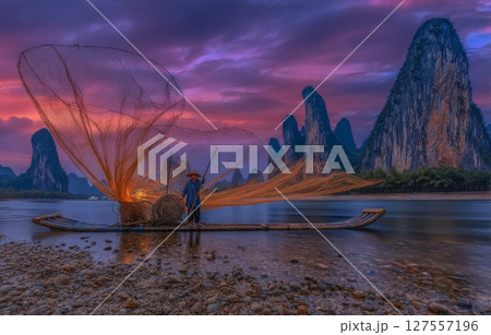 Xingping, China, is where a cormorant fisherman can be seen throwing a net from a traditional Chinese bamboo boat at the break of day 127557196