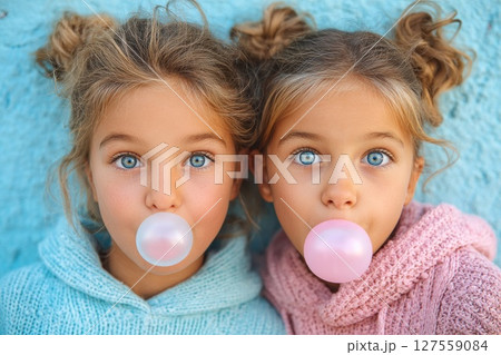 Twin Girls Blowing Bubblegum in Colorful Sweaters 127559084