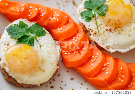 Fried eggs with meat cutlets and carrots with spices and sesame seeds, top view, close-up selective focus 127561058