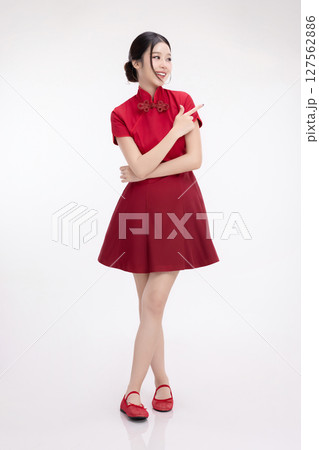 Full body portrait of joyful beauty Asian woman in red Cheongsam Chinese traditional dress celebrating and pointing finger to copy space isolated on white background. Full body portrait of joyful beauty Asian woman in red Cheongsam Chinese traditional dress celebrating and pointing finger to copy space isolated on white background. 127562886