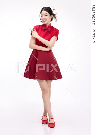 Full body portrait of joyful beauty Asian woman in red Cheongsam Chinese traditional dress celebrating and pointing finger to copy space isolated on white background. 127562888
