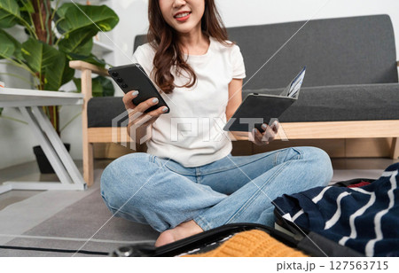 Travel Preparation and Digital Shopping. Young woman organizing suitcase while checking smartphone. 127563715