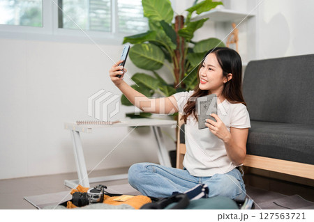 Selfie Moment Before Travel. Young woman capturing a joyful selfie while preparing her suitcase. 127563721