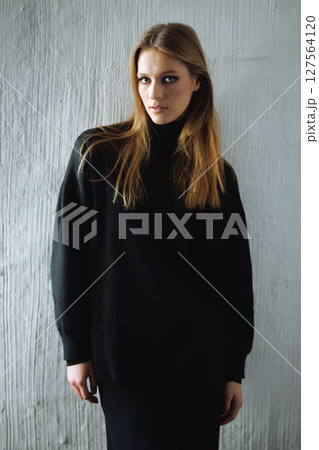 Moody sophistication concept - woman in a black sweater, bathed in soft shadows, her calm powerful gaze drawing you in as neutral tones and a textured white wall create a timeless cinematic atmosphere Moody sophistication concept - woman in a black sweater, bathed in soft shadows, her calm powerful gaze drawing you in as neutral tones and a textured white wall create a timeless cinematic atmosphere 127564120