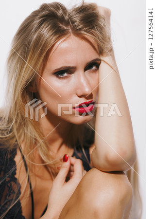 emotions and feelings concept - sensual blonde woman in lingerie, experiencing pure pleasure, body arching, mouth open in ecstasy, her glowing skin bathed in bright light against a white backdrop 127564141