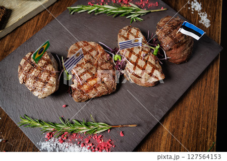 Juicy grilled steaks with Brazilian, Uruguayan, and Estonian flags. Served with fresh herbs and microgreens on a slate plate, showcasing international gourmet cuisine in a fine dining setting Juicy grilled steaks with Brazilian, Uruguayan, and Estonian flags. Served with fresh herbs and microgreens on a slate plate, showcasing international gourmet cuisine in a fine dining setting 127564153